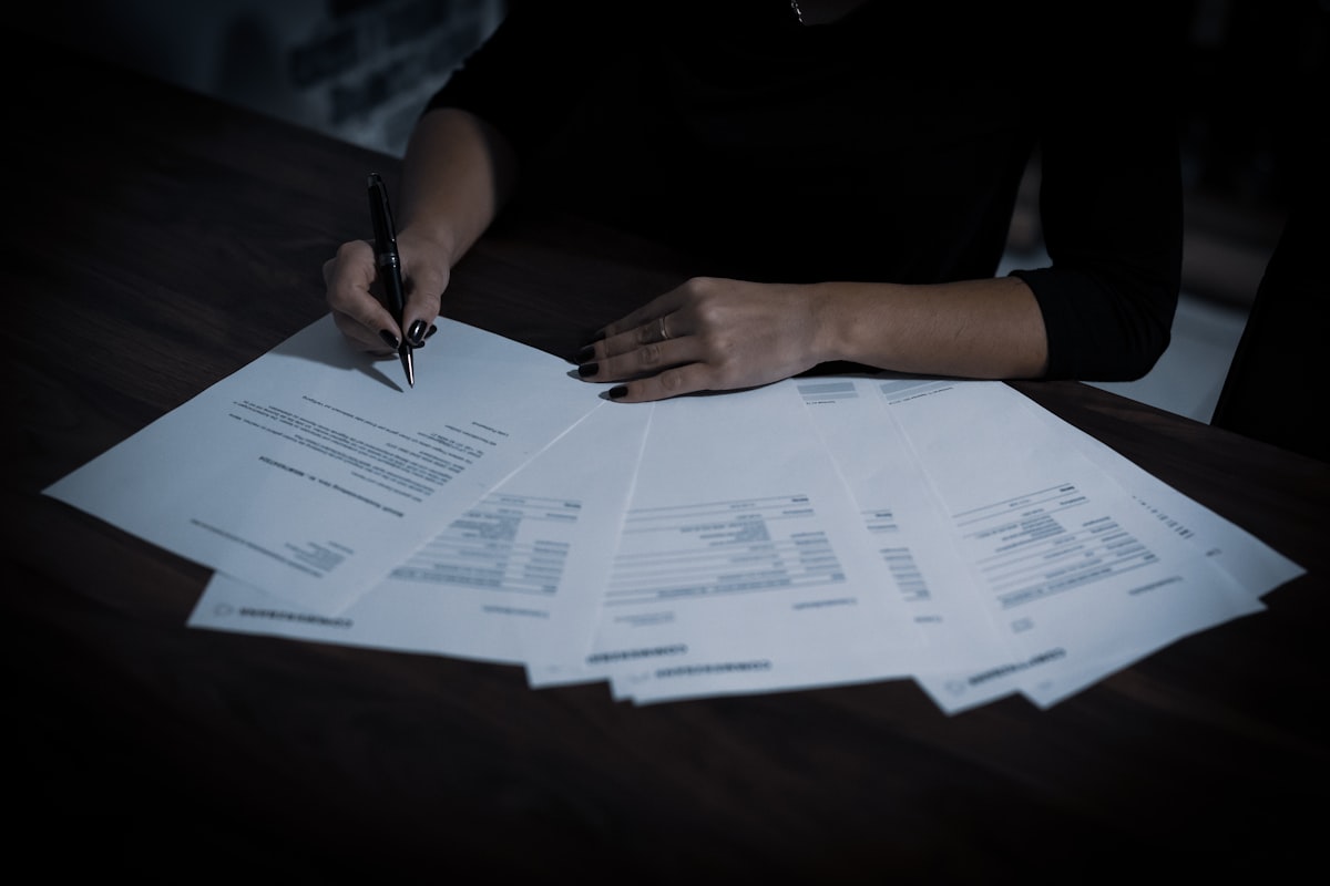 Compliance officer reviewing a spread of audit documents at a desk, pen in hand