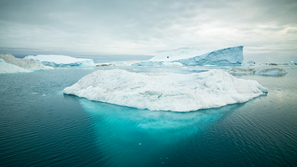 An Arctic iceberg on still water, with the much larger submerged mass glowing turquoise beneath the waterline