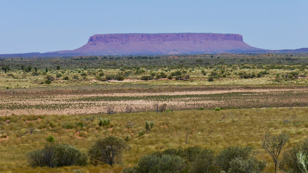 A single flat-topped mountain rising above dry grassland under a clear sky, its summit a long level plateau